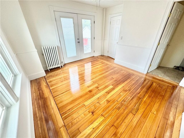 unfurnished bedroom with radiator, french doors, baseboards, light wood-style flooring, and access to outside