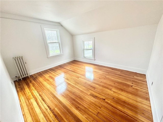 bonus room with light wood-type flooring, vaulted ceiling, baseboards, and radiator heating unit