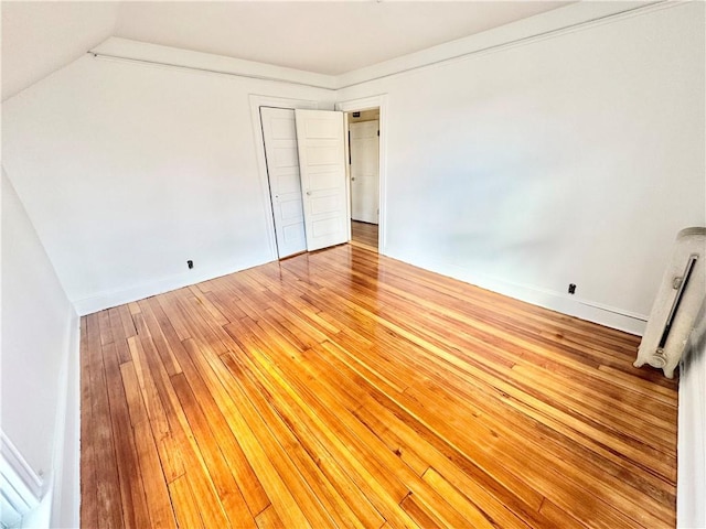 unfurnished bedroom with light wood finished floors, a closet, baseboards, lofted ceiling, and radiator heating unit