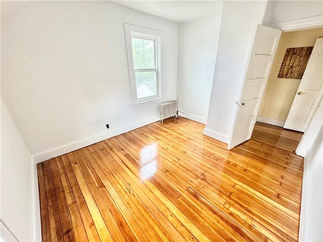spare room featuring baseboards, radiator, and light wood finished floors