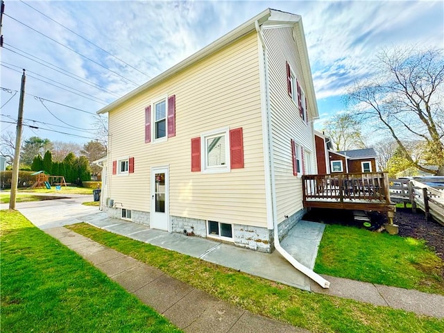 view of property exterior featuring a playground, a deck, and a lawn