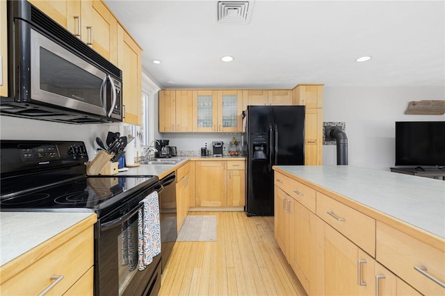 kitchen with glass insert cabinets, light brown cabinetry, light wood-style floors, black appliances, and a sink