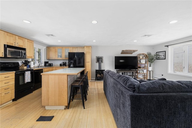 kitchen with a kitchen bar, black appliances, light brown cabinets, and open floor plan