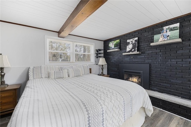 bedroom with a brick fireplace, beamed ceiling, wood finished floors, and crown molding