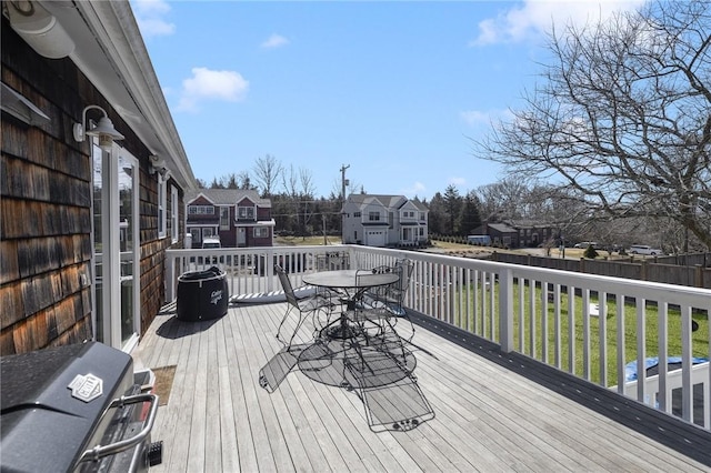 wooden deck with outdoor dining space, a lawn, a grill, and a residential view