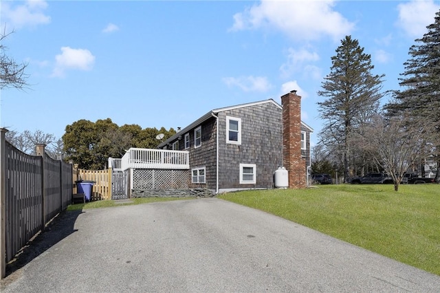 exterior space featuring fence, a yard, a chimney, a deck, and aphalt driveway