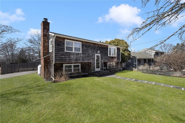 back of house featuring entry steps, a yard, fence, and a chimney