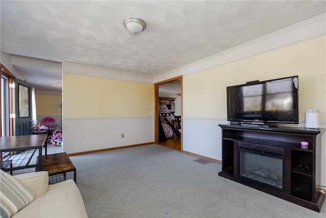 carpeted living room with a glass covered fireplace, baseboards, and ornamental molding