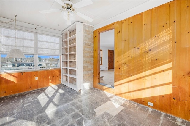 spare room featuring a baseboard heating unit, wooden walls, and ceiling fan