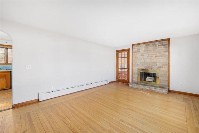 unfurnished living room with a baseboard radiator, baseboards, light wood-style floors, and a stone fireplace