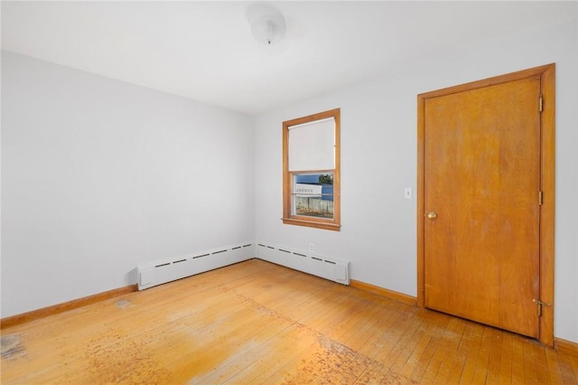 empty room featuring a baseboard heating unit, light wood-type flooring, and baseboards