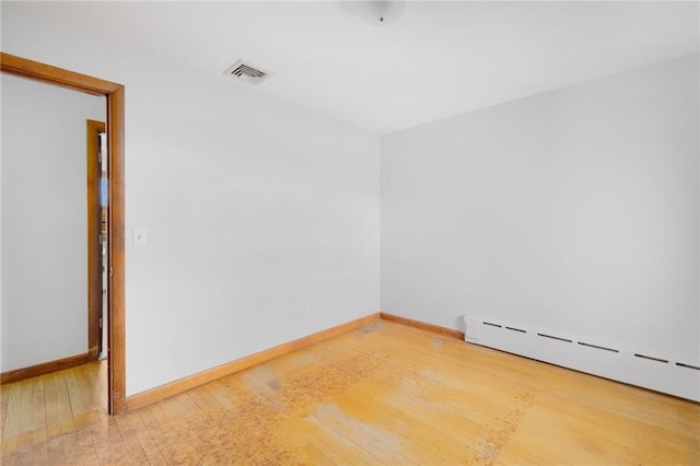 empty room with visible vents, a baseboard heating unit, baseboards, and hardwood / wood-style floors