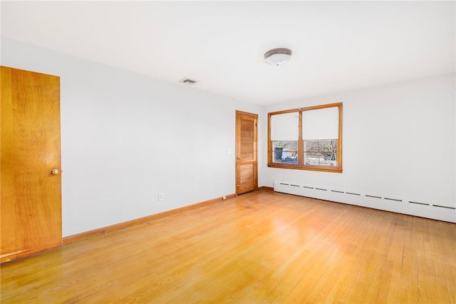 unfurnished room featuring baseboard heating, baseboards, visible vents, and light wood finished floors