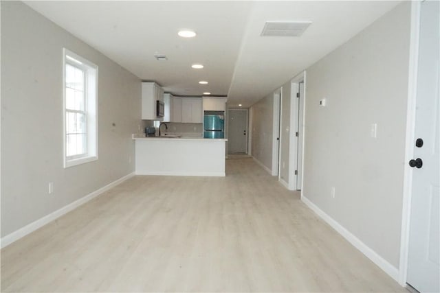 unfurnished living room with recessed lighting, baseboards, light wood-type flooring, and a sink