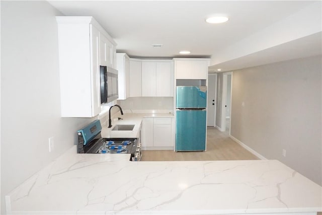 kitchen featuring light stone counters, white cabinets, stainless steel appliances, and a sink