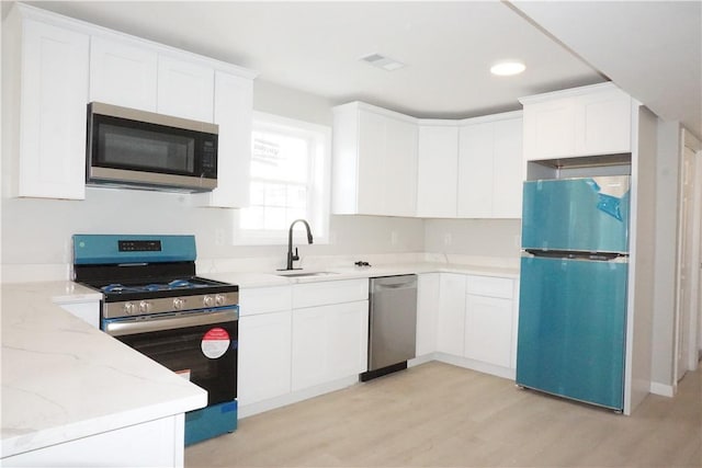 kitchen with light wood finished floors, light stone countertops, stainless steel appliances, white cabinetry, and a sink