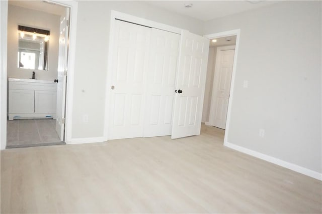 unfurnished bedroom with baseboards, light wood finished floors, a sink, a closet, and ensuite bathroom