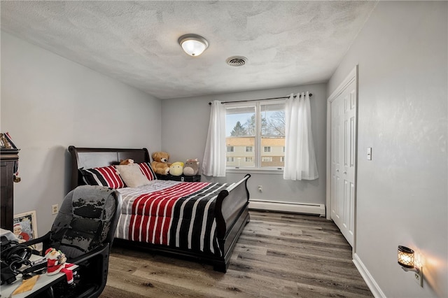 bedroom with visible vents, a baseboard heating unit, a textured ceiling, wood finished floors, and baseboards