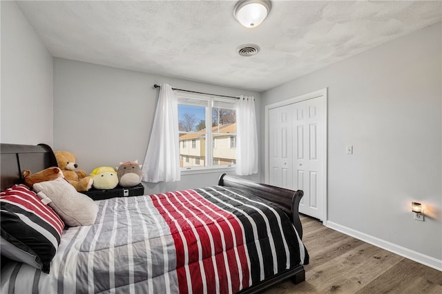 bedroom with visible vents, baseboards, wood finished floors, a closet, and a textured ceiling