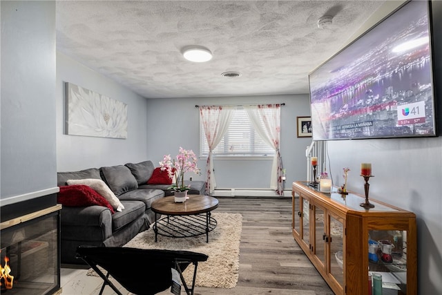 living room with wood finished floors, visible vents, baseboard heating, and a textured ceiling