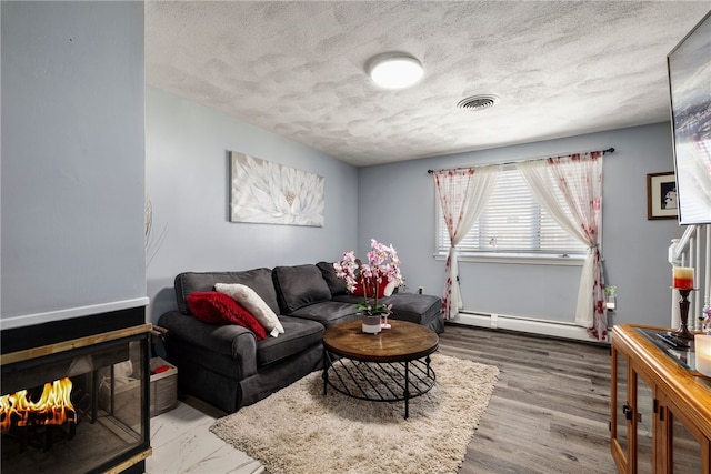 living room featuring visible vents, a textured ceiling, baseboard heating, and wood finished floors