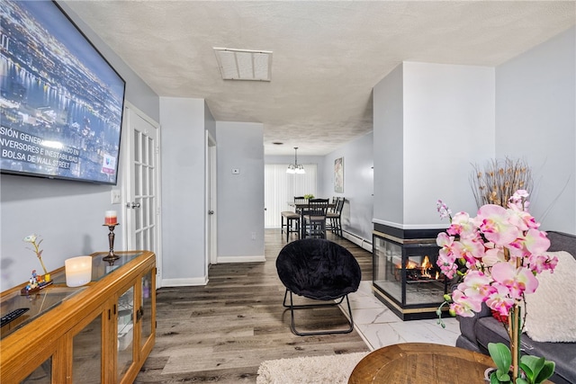 living area with visible vents, baseboards, wood finished floors, a notable chandelier, and a textured ceiling