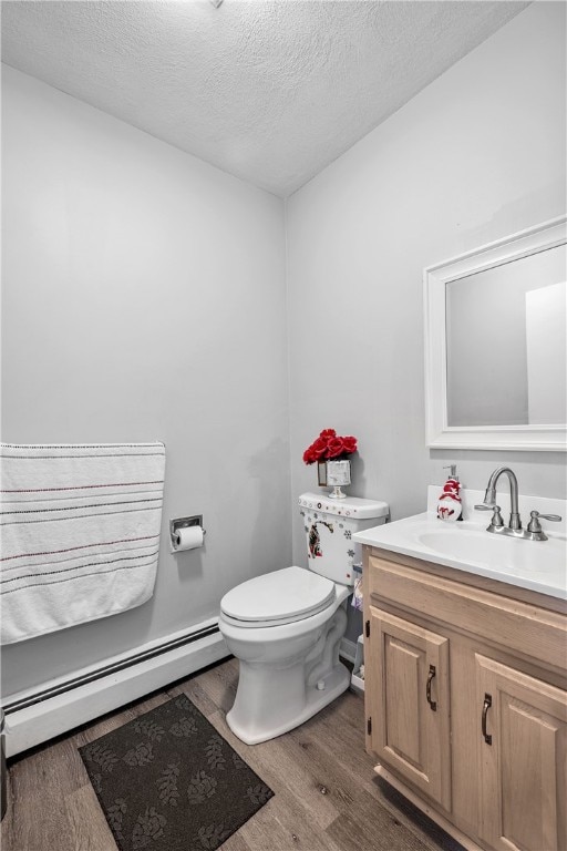 half bathroom featuring toilet, vanity, wood finished floors, a textured ceiling, and a baseboard radiator