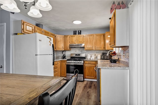 kitchen with under cabinet range hood, wood finished floors, freestanding refrigerator, decorative backsplash, and stainless steel range with gas stovetop