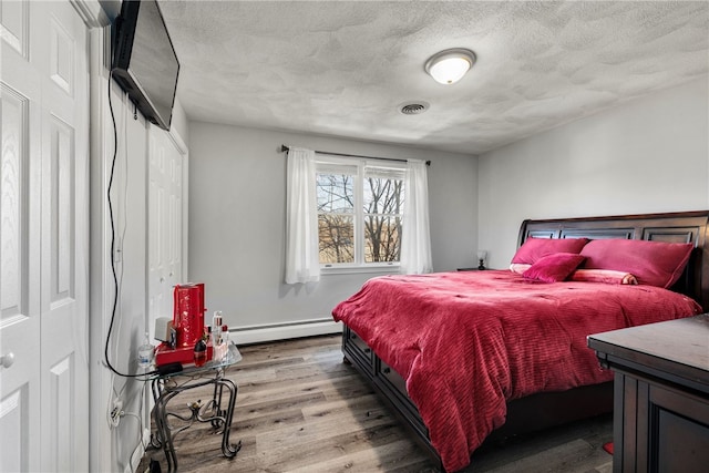 bedroom featuring wood finished floors, baseboards, visible vents, a baseboard radiator, and a textured ceiling