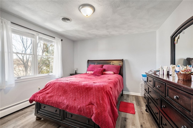 bedroom featuring baseboard heating, a textured ceiling, visible vents, and wood finished floors