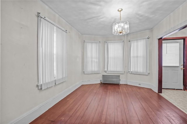 spare room with hardwood / wood-style floors, a notable chandelier, radiator, and baseboards