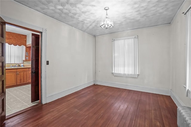 spare room with radiator, hardwood / wood-style floors, baseboards, and a sink