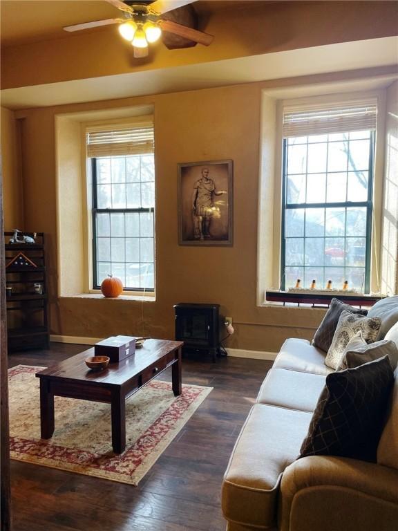 living room with dark wood-style floors, a ceiling fan, a wood stove, and baseboards