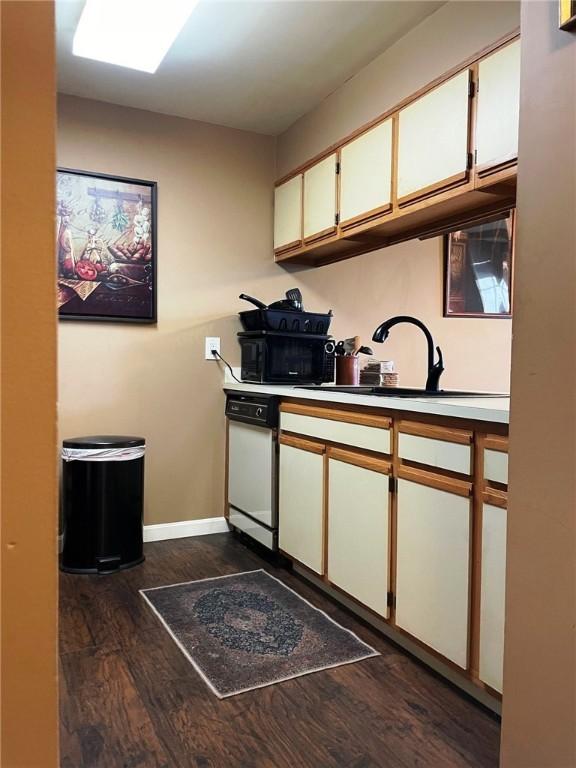 kitchen featuring a sink, black microwave, white dishwasher, white cabinets, and dark wood-style flooring