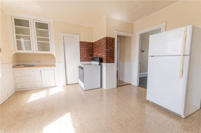 kitchen with white appliances, light floors, a wainscoted wall, washer / dryer, and glass insert cabinets