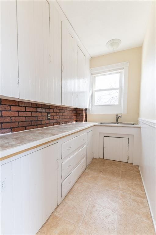 kitchen with light tile patterned floors, white cabinets, light countertops, and a sink