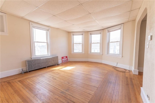 spare room featuring a paneled ceiling, arched walkways, wood-type flooring, and radiator heating unit