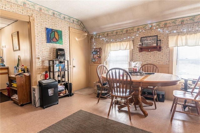 dining area featuring lofted ceiling, a healthy amount of sunlight, tile patterned floors, and wainscoting