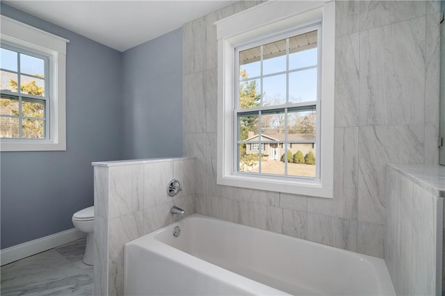 bathroom featuring baseboards, toilet, marble finish floor, and a bath