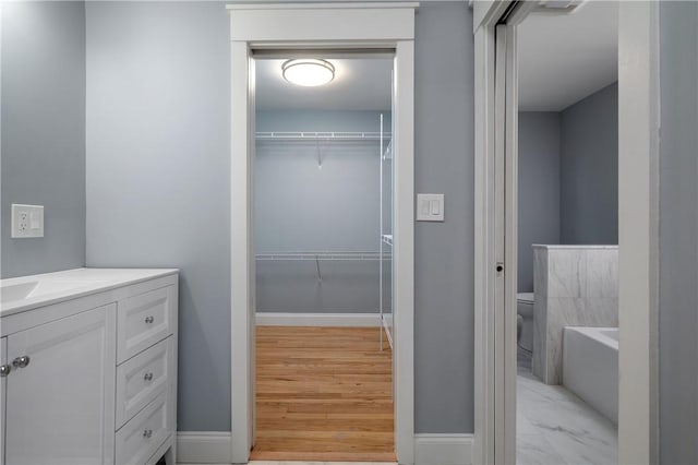 full bathroom with toilet, a walk in closet, and baseboards