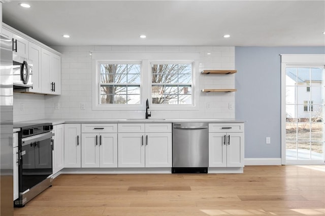 kitchen with a sink, white cabinetry, appliances with stainless steel finishes, light wood finished floors, and decorative backsplash