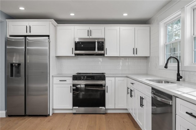 kitchen with a sink, appliances with stainless steel finishes, light wood-style flooring, and white cabinetry