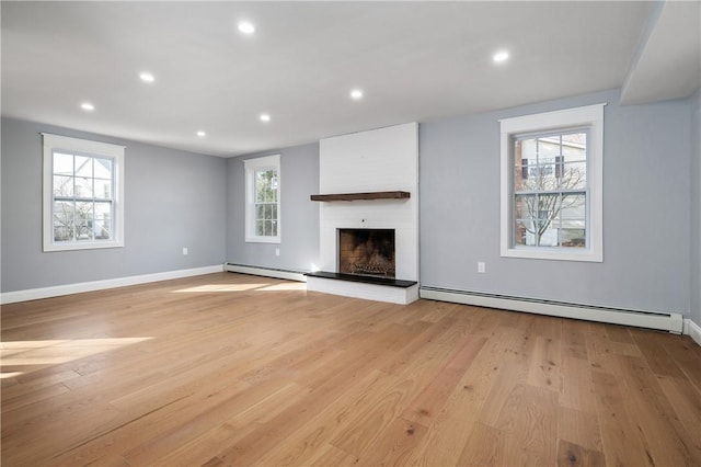 unfurnished living room with a baseboard heating unit, recessed lighting, a fireplace with raised hearth, and light wood-style floors