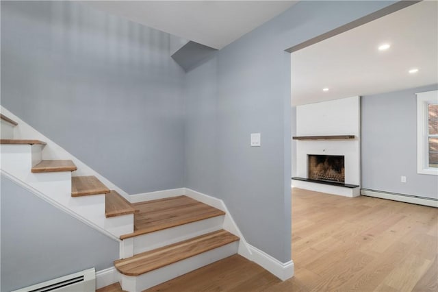 stairway featuring wood finished floors, recessed lighting, a large fireplace, baseboards, and baseboard heating