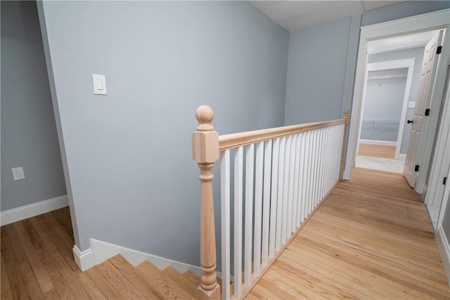 hallway featuring baseboards, light wood-style floors, and an upstairs landing