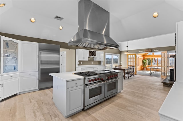 kitchen with high end appliances, visible vents, lofted ceiling, white cabinets, and island range hood