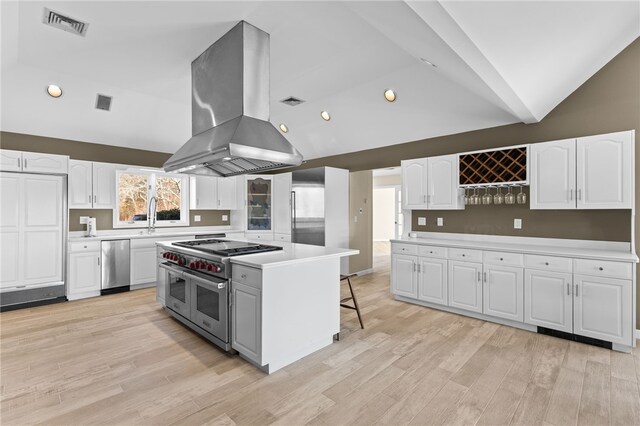 kitchen with lofted ceiling, island exhaust hood, white cabinets, appliances with stainless steel finishes, and a kitchen bar