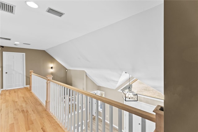 corridor with visible vents, light wood finished floors, and vaulted ceiling