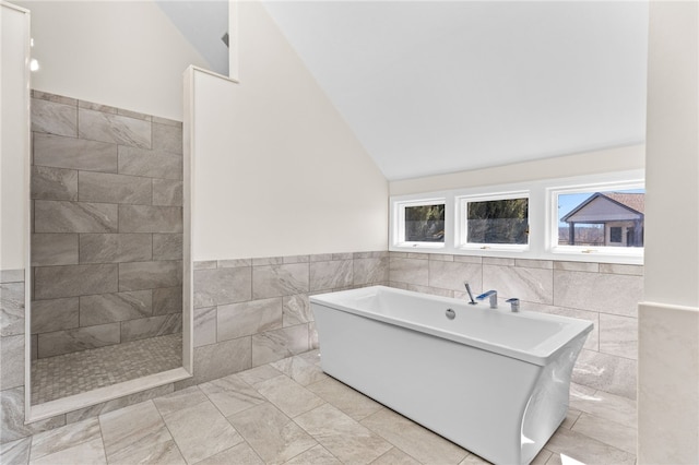 full bathroom featuring tile walls, a soaking tub, lofted ceiling, and wainscoting