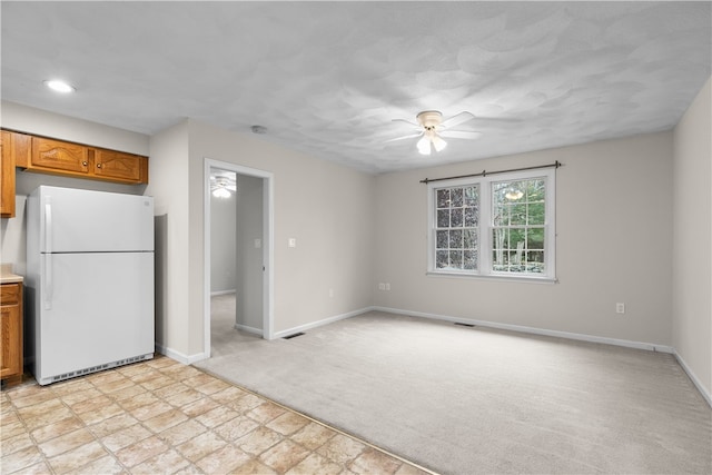 kitchen with baseboards, ceiling fan, light colored carpet, freestanding refrigerator, and brown cabinetry